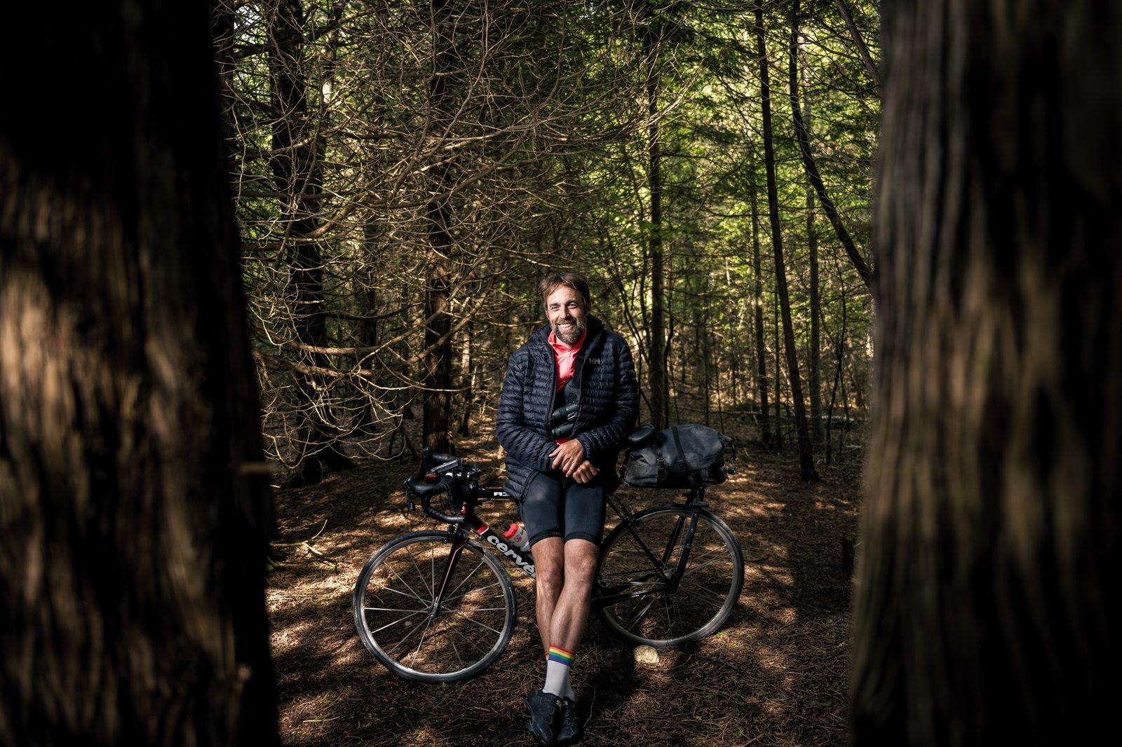 Brett Forsyth smiling, leaning on his loaded road bike in a cedar forest during his 2022 human-powered Big Year